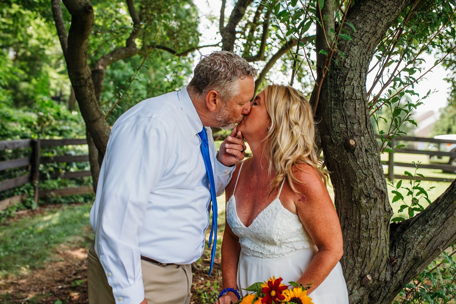 A romantic moment unfolds in a sunlit garden setting with lush greenery and trees.