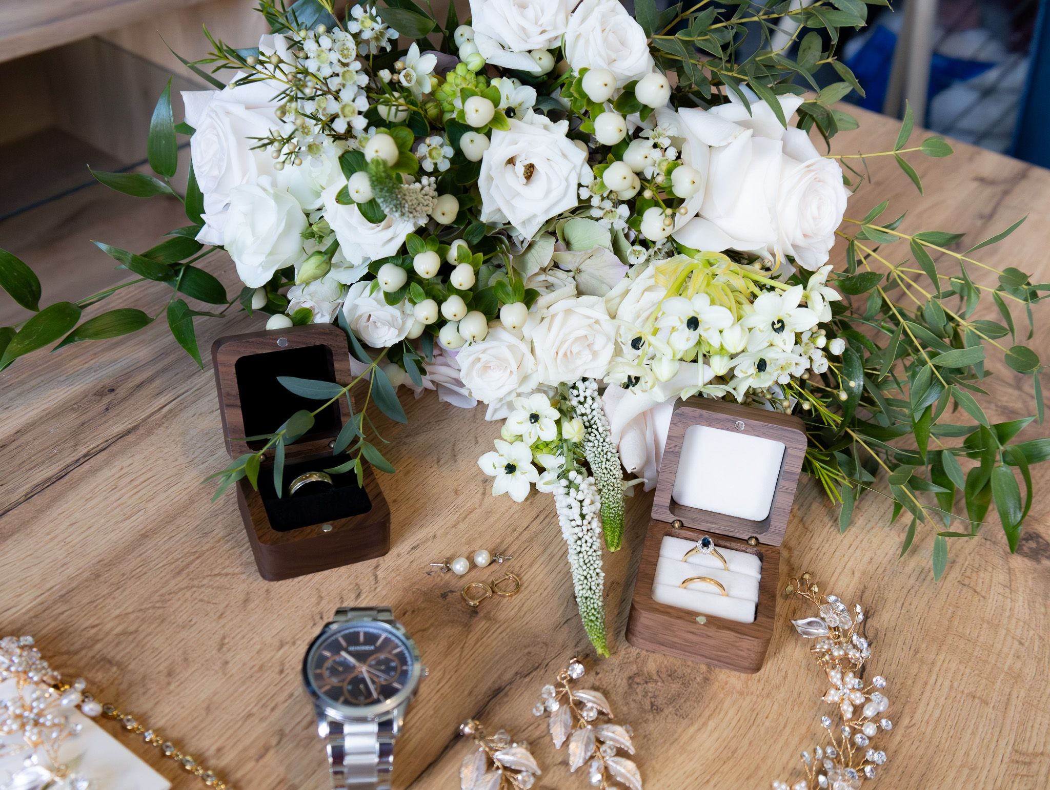 Wedding details including rings, flowers, and accessories arranged on a rustic wooden surface with elegant styling.