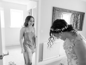 A candid black and white wedding preparation moment showing an emotional reaction in a bright room with a mirror.