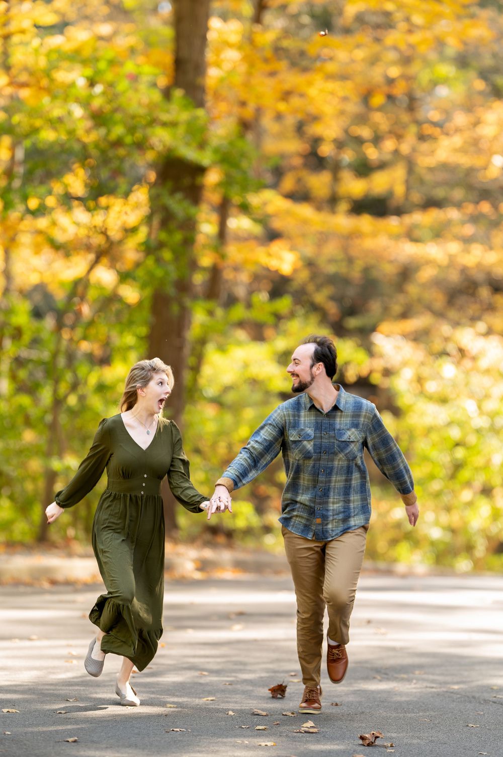 Laughing couple holding hands and running together on a path with bright autumn trees.