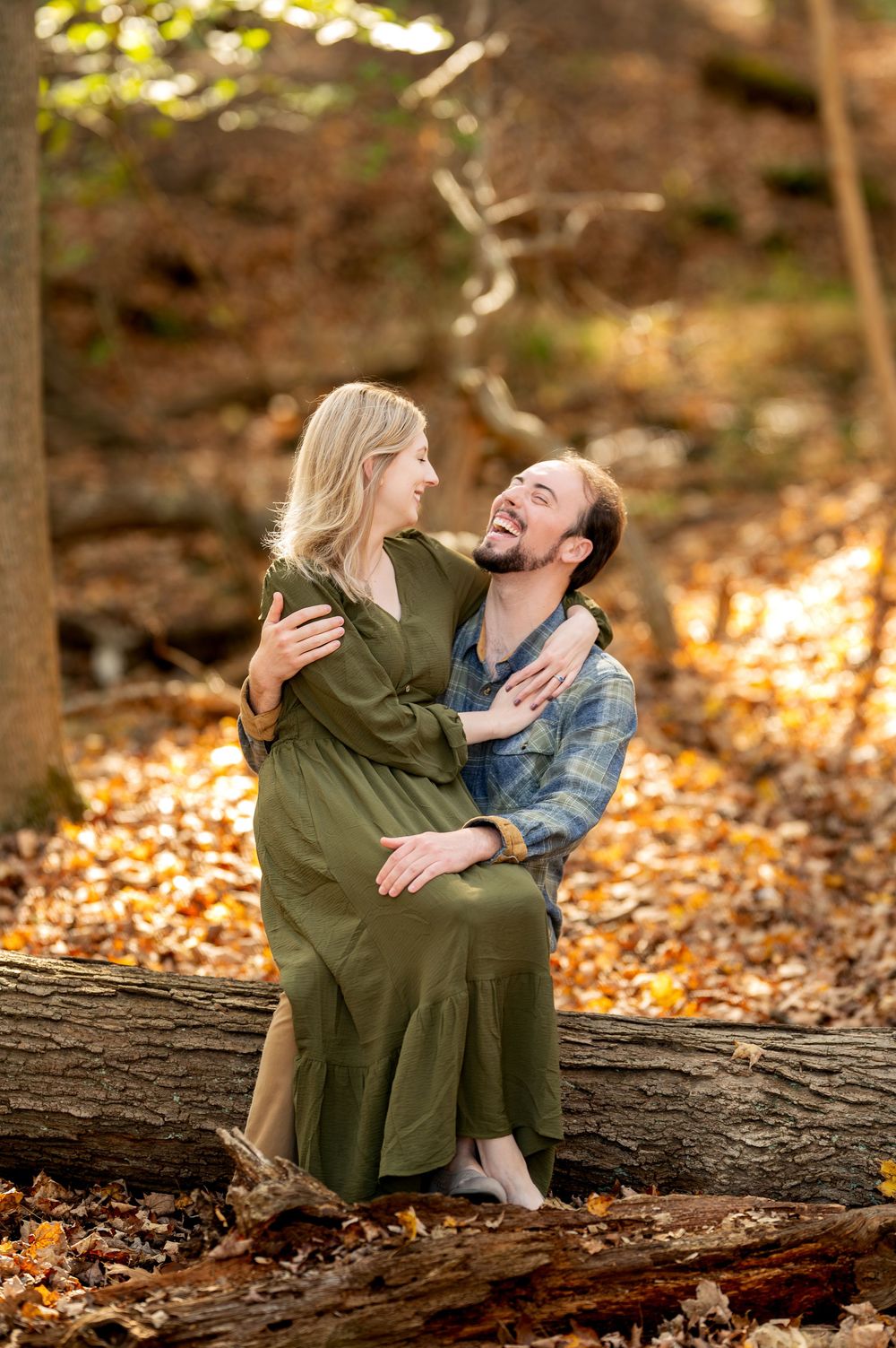 Couple laughing and embracing on a fallen log in an autumn forest with golden leaves.