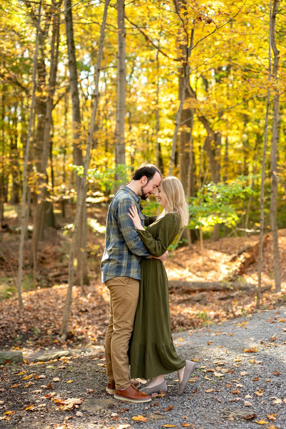 Couple sharing a kiss while embracing on a gravel path in a colorful fall forest.