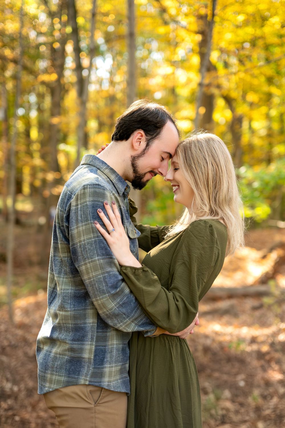 Happy couple touching foreheads and embracing in a sunlit golden autumn forest.