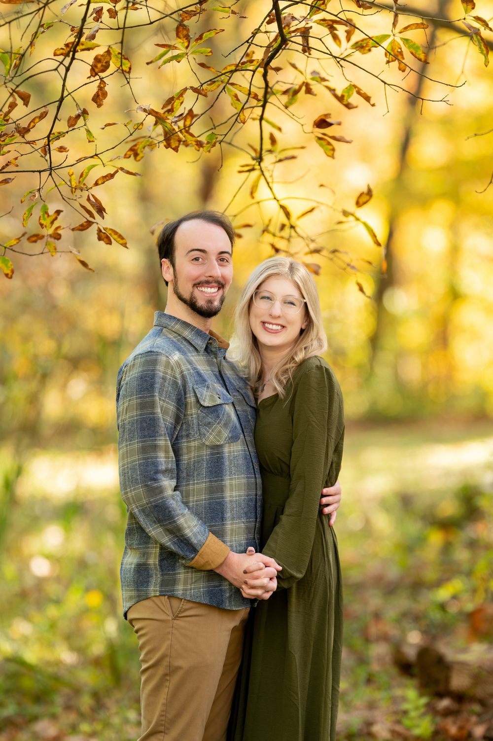 Smiling couple embracing under fall foliage branches in a golden autumn forest.