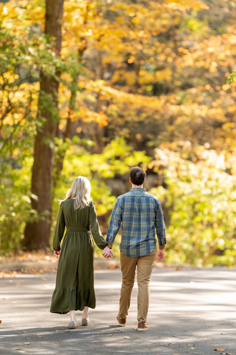 Couple walking hand in hand down a path through a vibrant autumn forest.