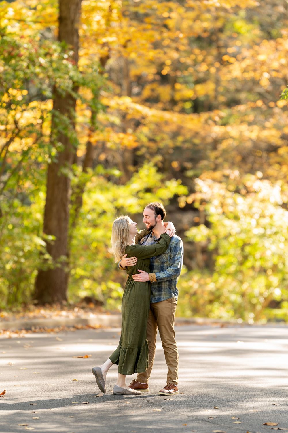 Happy couple embracing on a tree-lined path surrounded by vibrant yellow autumn foliage.