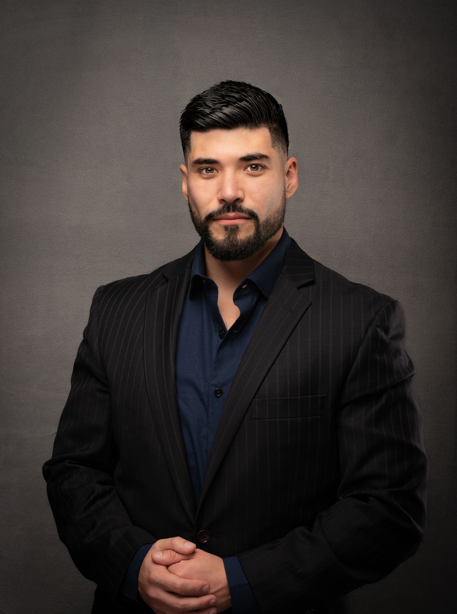 Confident businessman in a dark pinstripe suit posing against a neutral gray studio background.