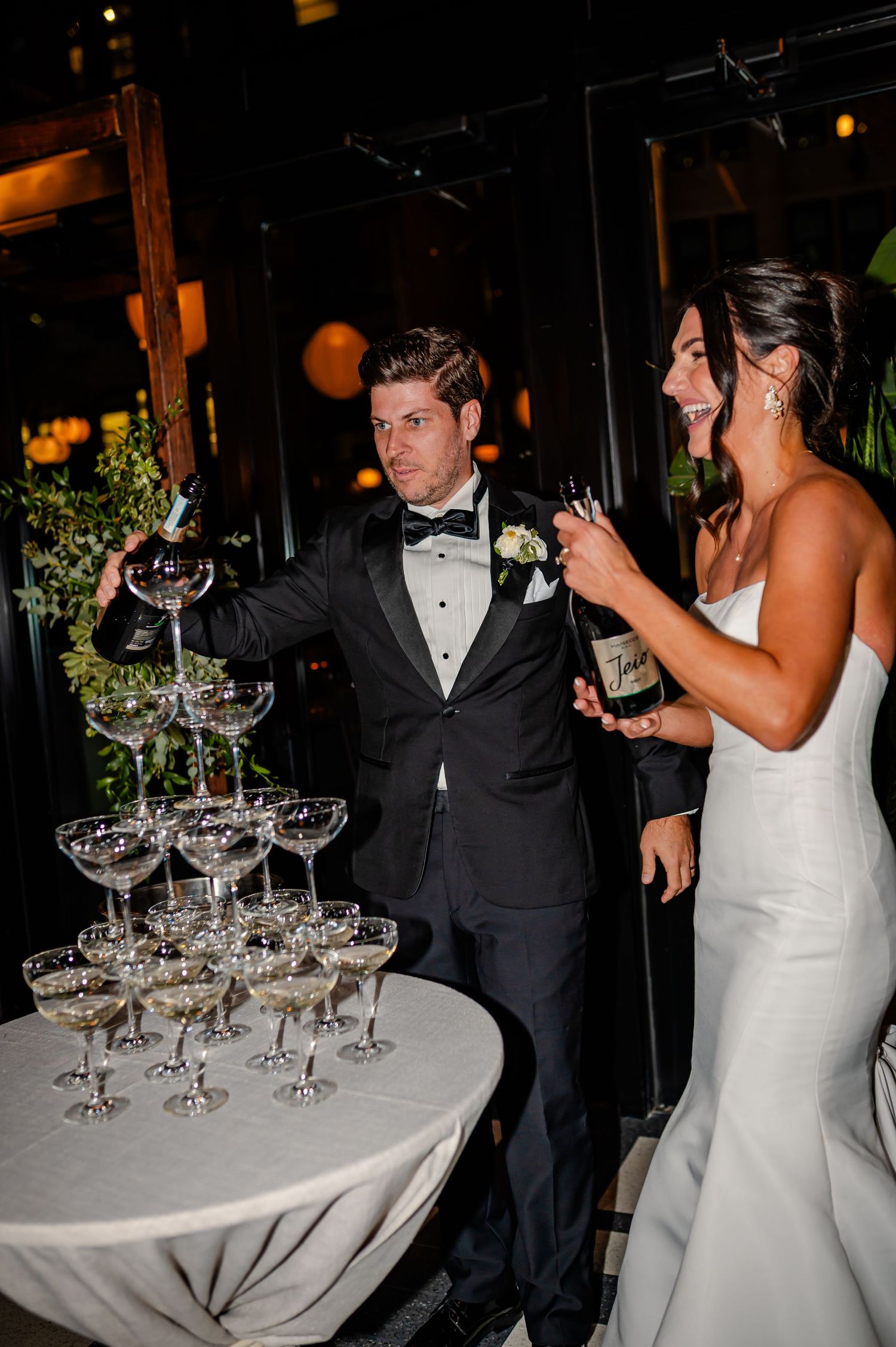 Wedding couple pours champagne into a tower of crystal glasses during their reception celebration.
