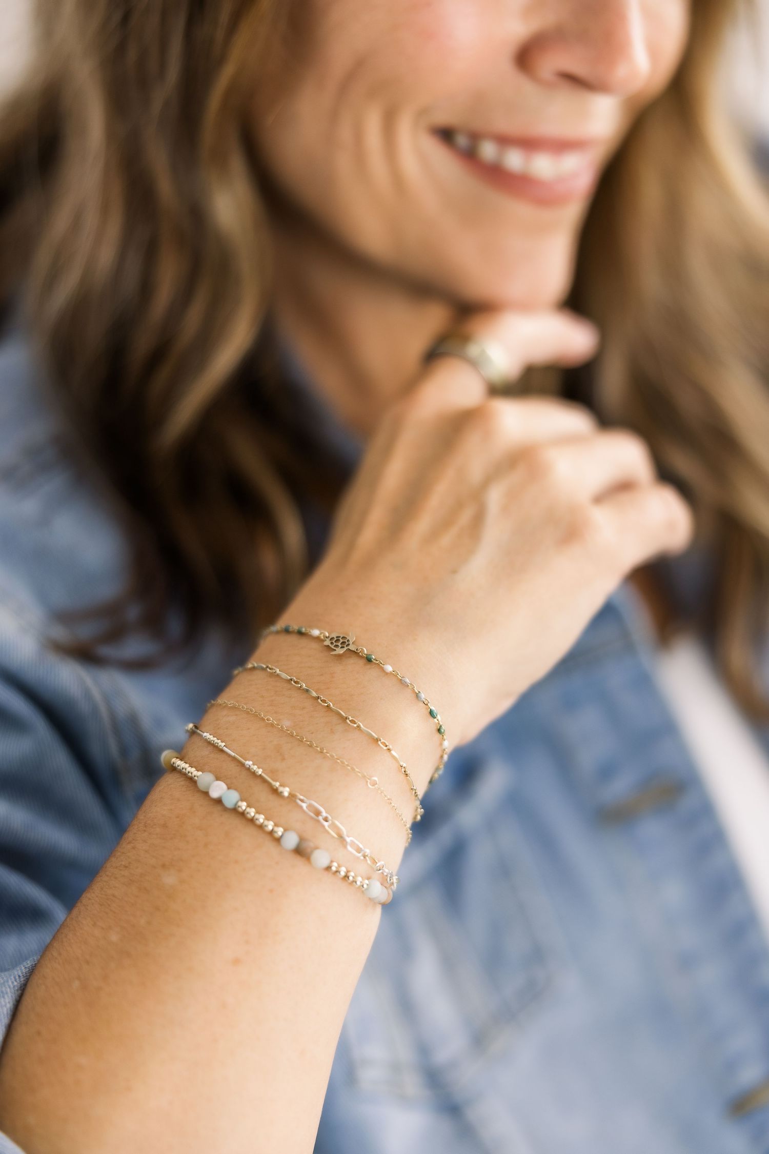Close-up view of delicate layered chain bracelets with crystal accents on a wrist against a denim background.