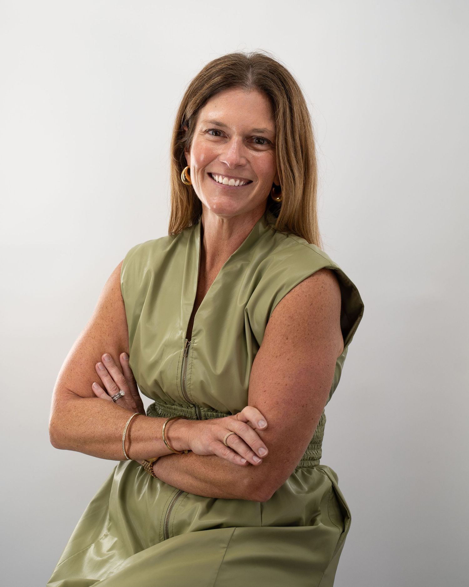 Person in a sleeveless olive green top poses with crossed arms against a white background in a photo series.