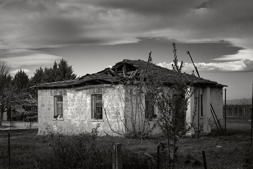 A panoramic black and white view of abandoned rural buildings against a dramatic cloudy sky.