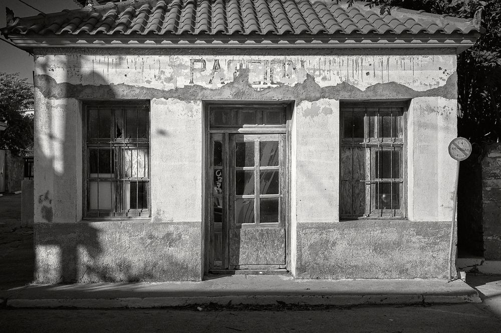 A row of weathered buildings with tiled roofs and peeling paint facades line an old street in black and white.