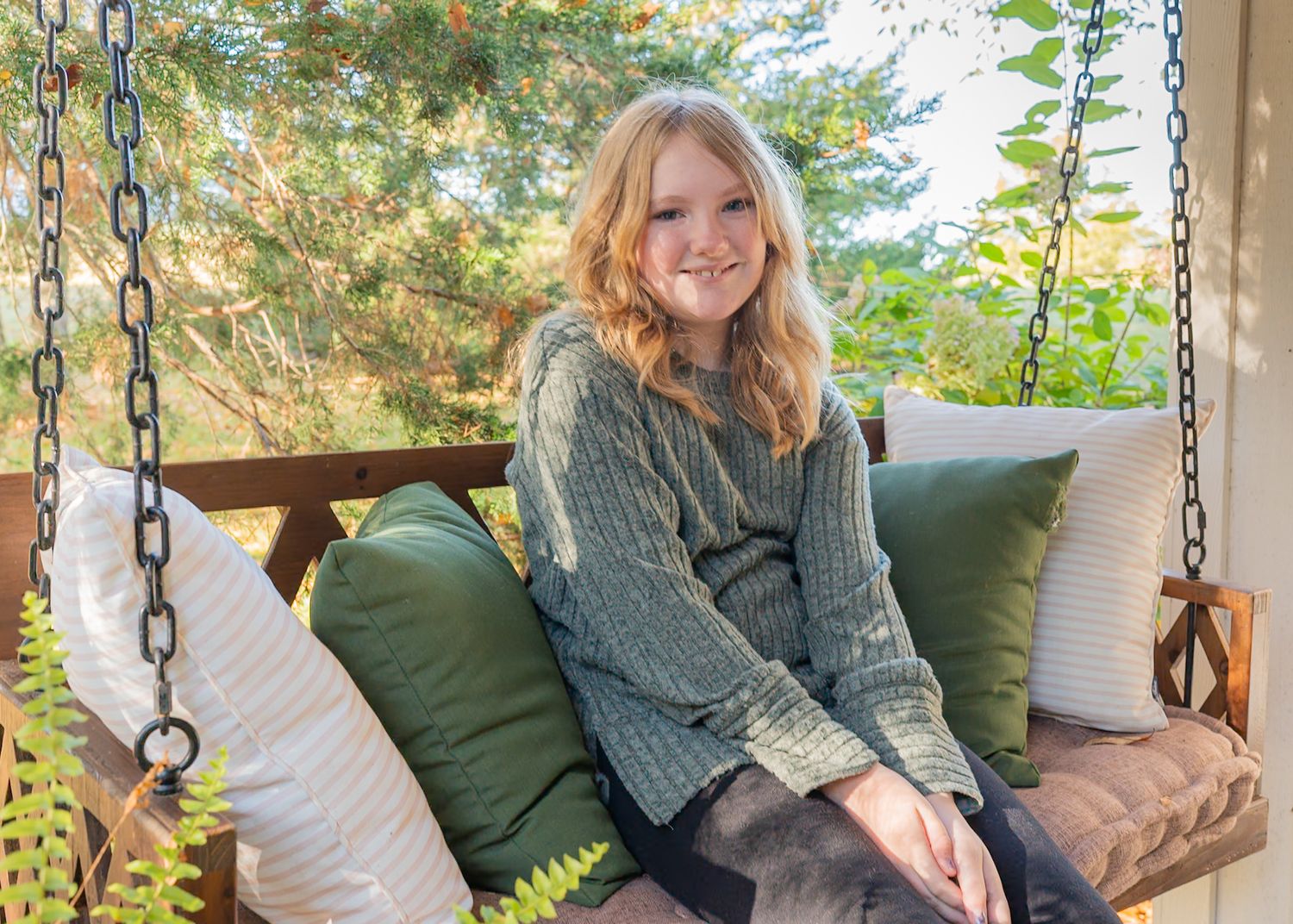 A cozy outdoor porch scene with green cushions and hanging chain swings in natural sunlight.