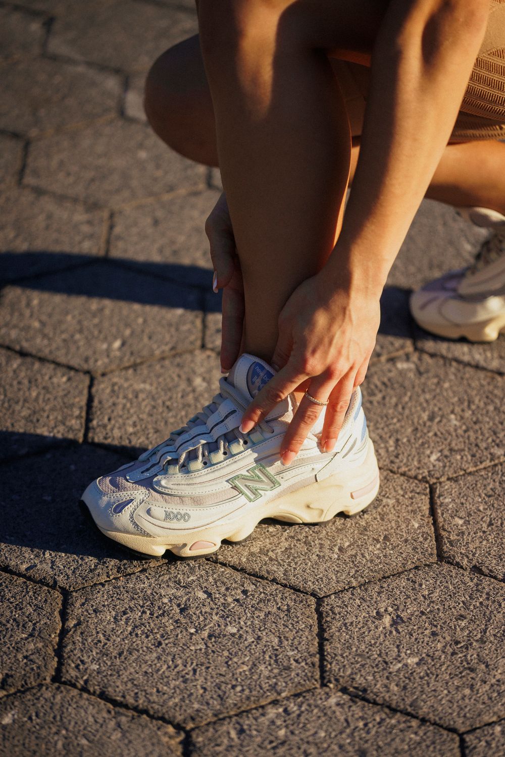 Close-up sequence showing hands adjusting and tying white New Balance sneakers on paved ground.