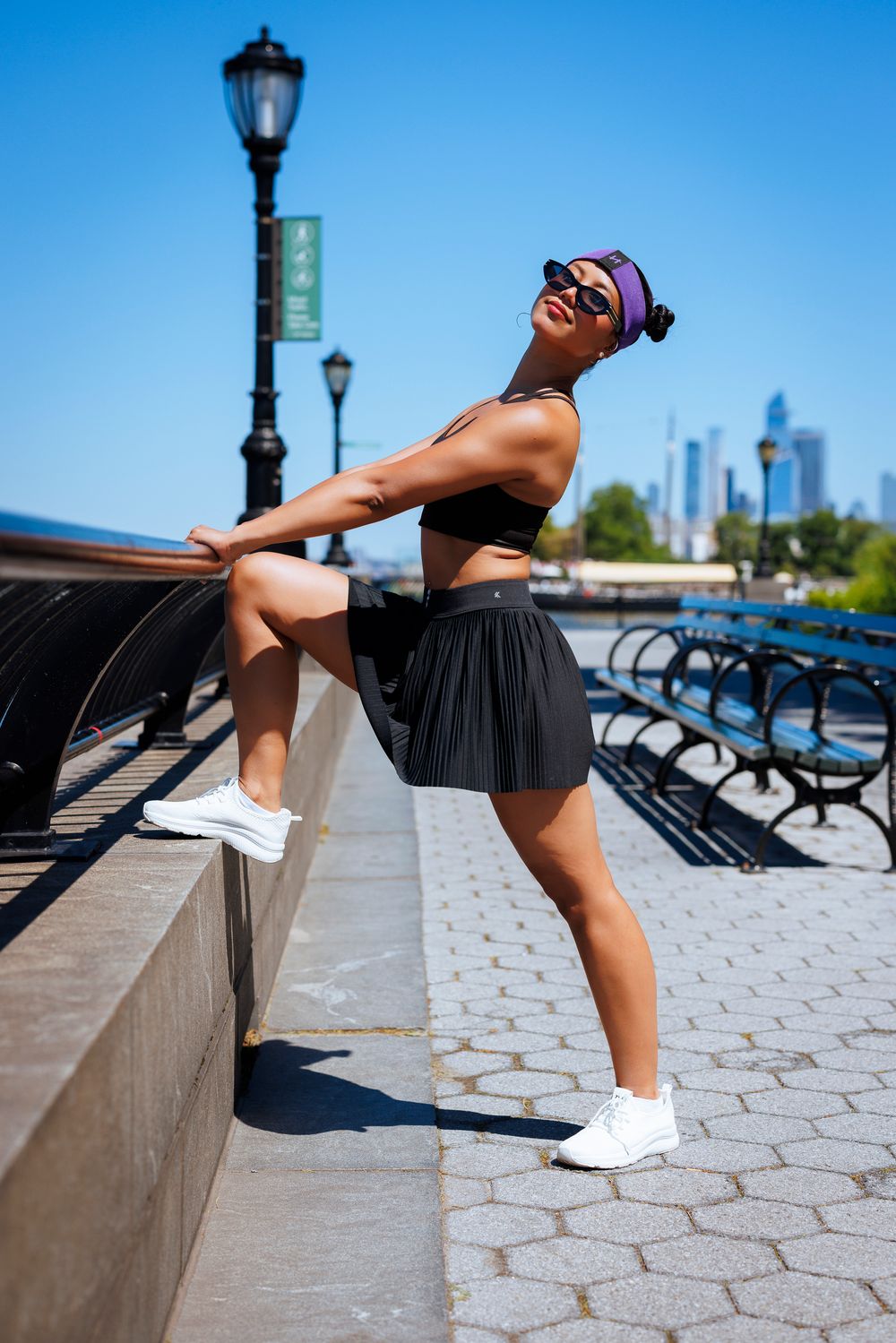 Athletic person in black shorts stretches leg on concrete ledge during outdoor workout with city skyline in background.