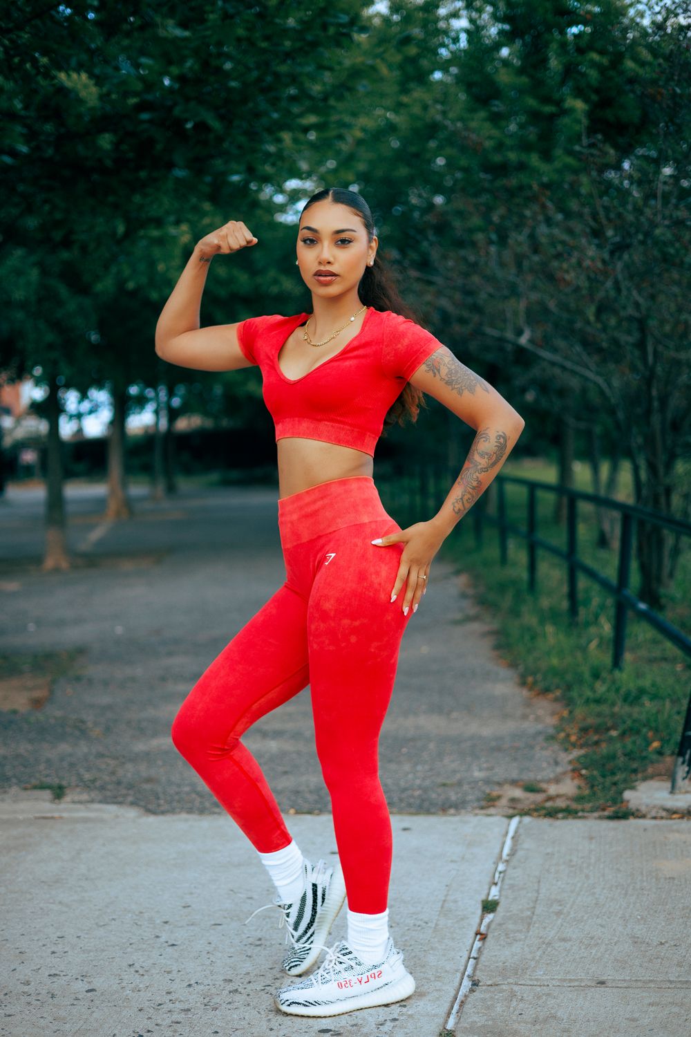 Dancer in bright red athletic wear strikes dynamic poses on a tree-lined path during an outdoor photoshoot.