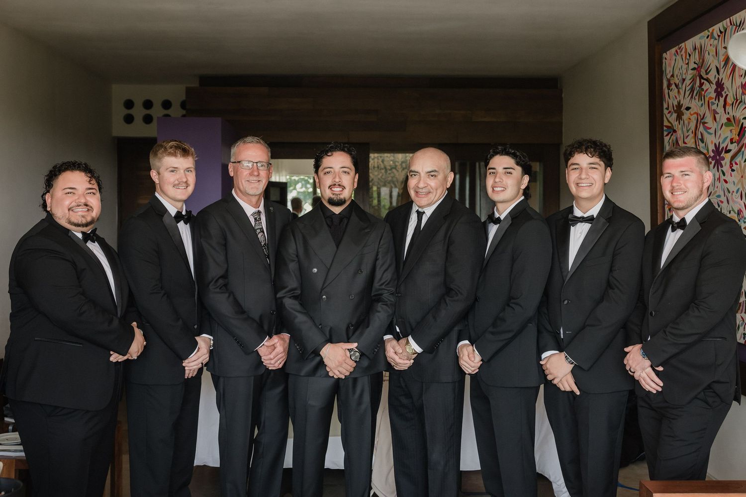 Group of groomsmen in formal black suits and bowties lined up for a photo.