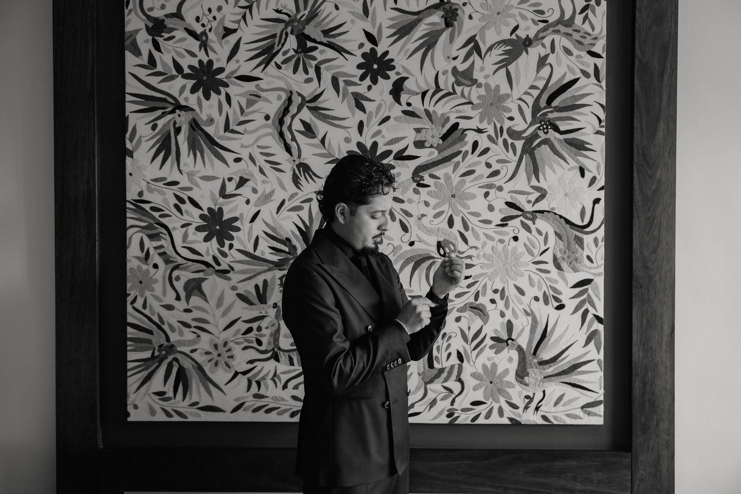 A silhouetted figure stands against a decorative floral wallpaper background in black and white.