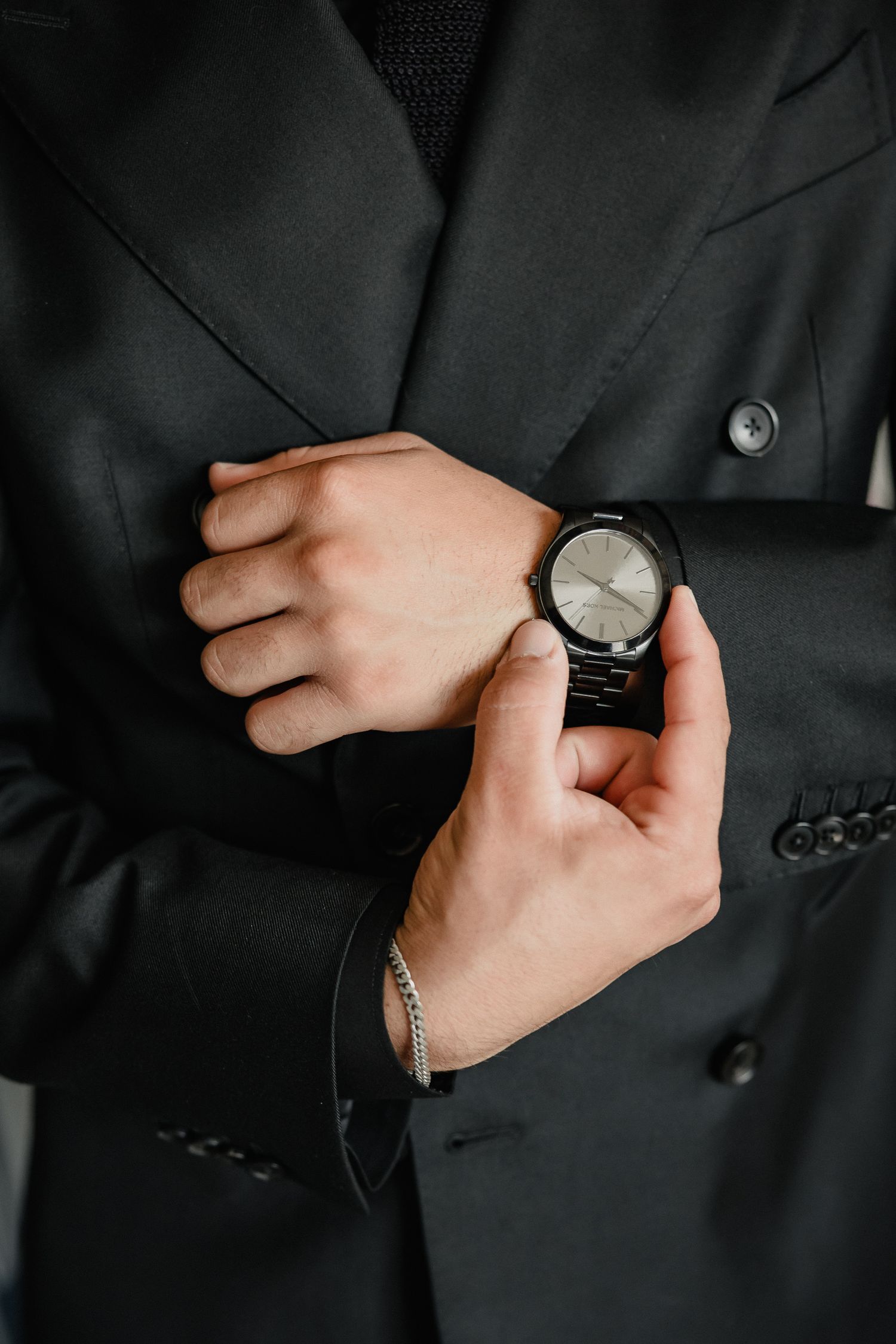Close-up details of a black suit sleeve with watch and cufflinks.