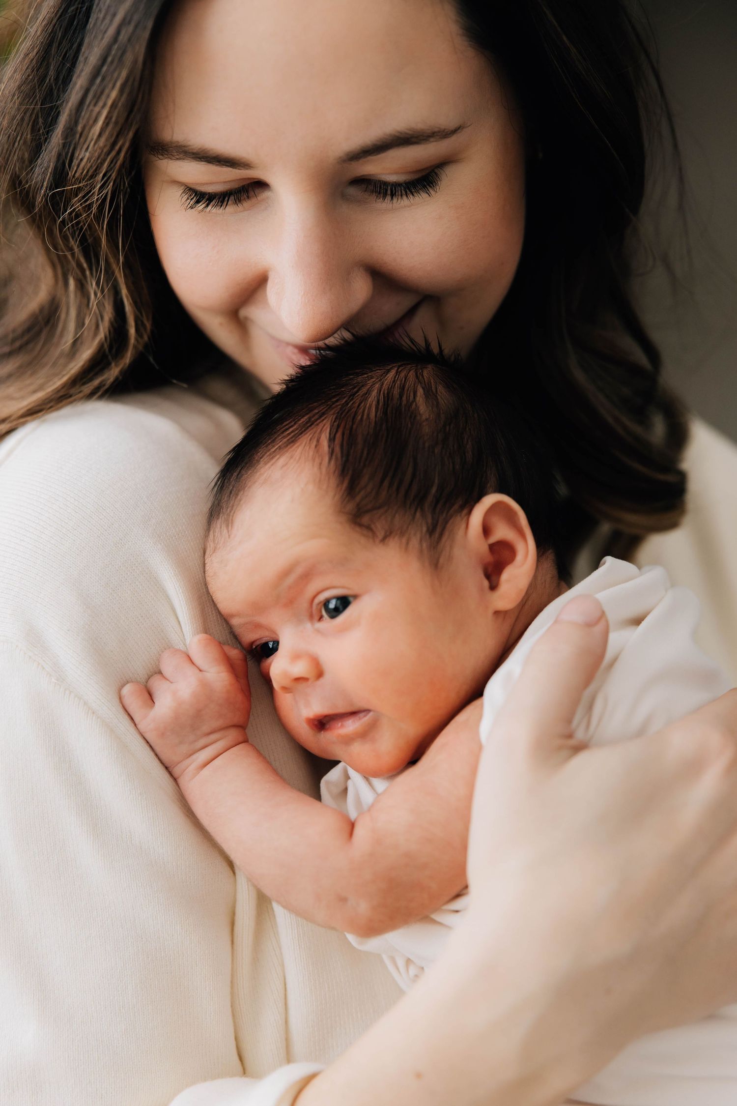 Smiling mother tenderly holding and nuzzling her newborn baby wrapped in white cloth.