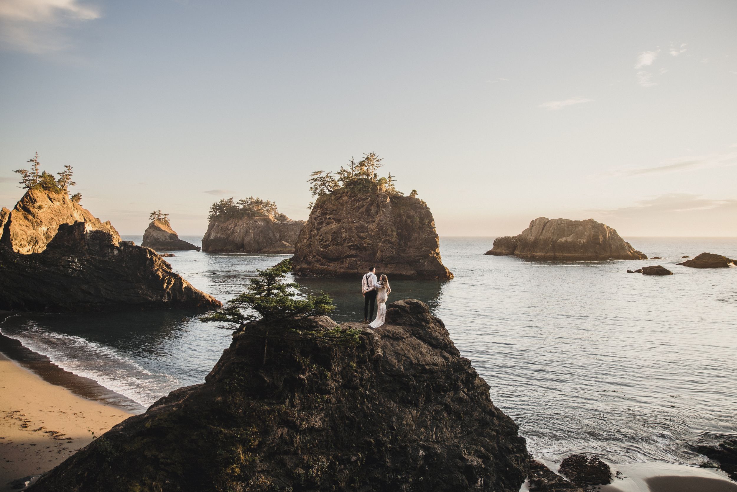 A romantic sunset photoshoot at a rocky coastal beach with dramatic cliffs and ocean views.