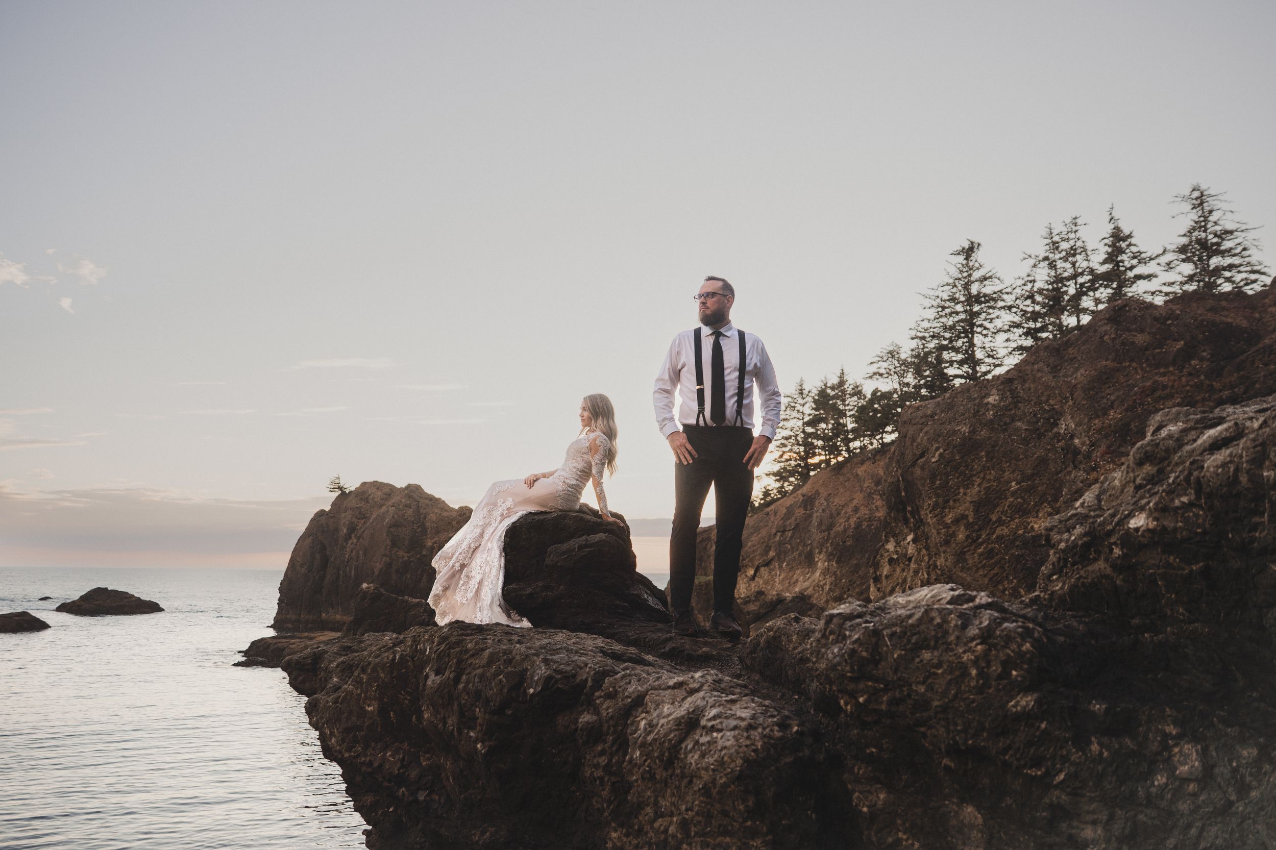 Silhouettes against a misty coastal landscape with rugged cliffs and evergreen trees at sunset.