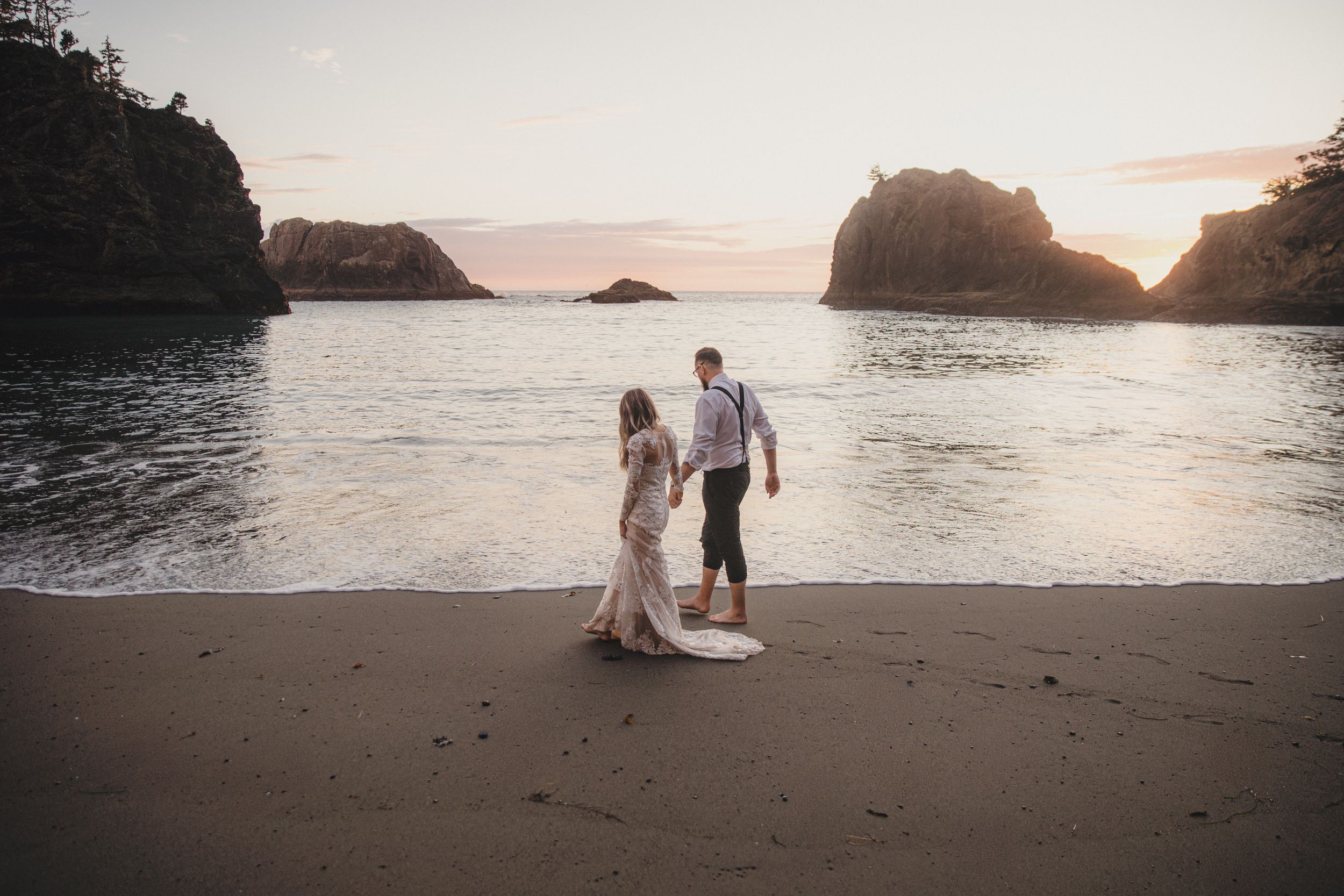 Couple walking along a dramatic coastline with rocky outcrops during golden hour.