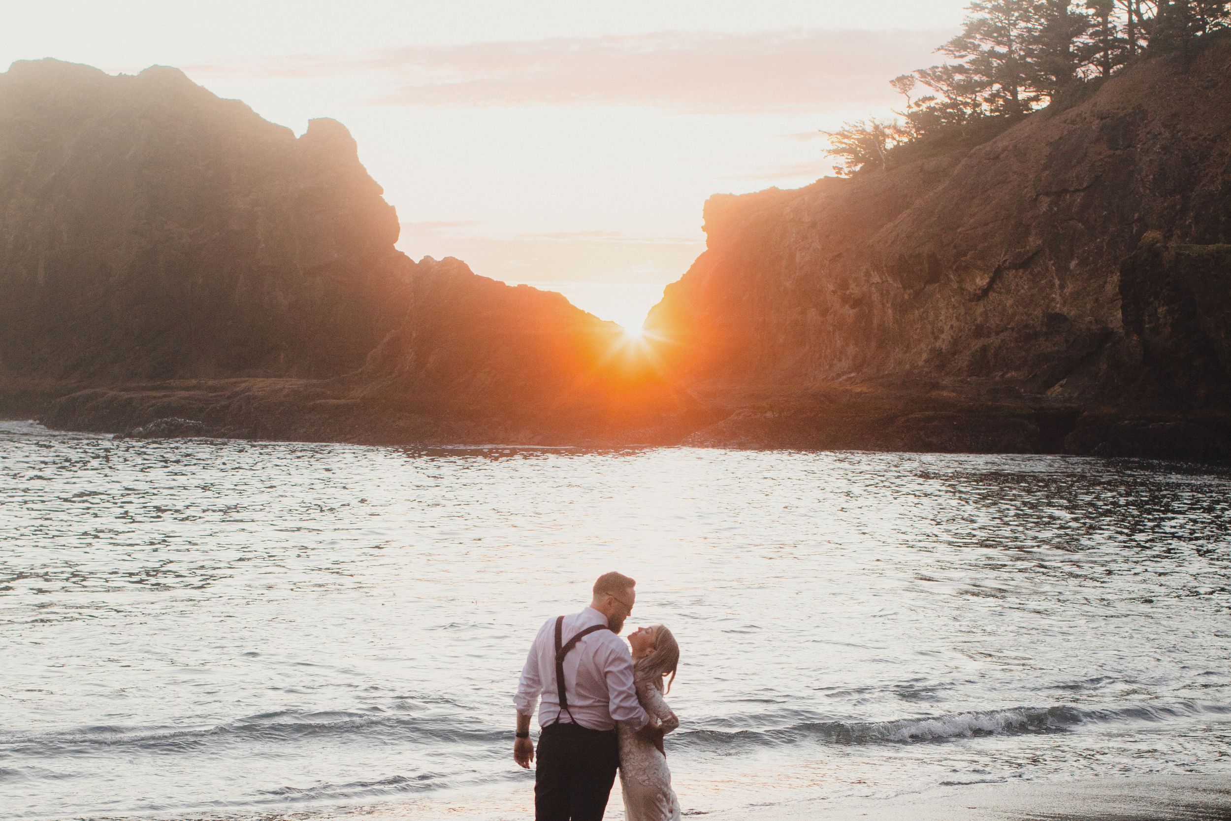 Sunset beach scene with waves crashing against rocky cliffs and warm evening light.