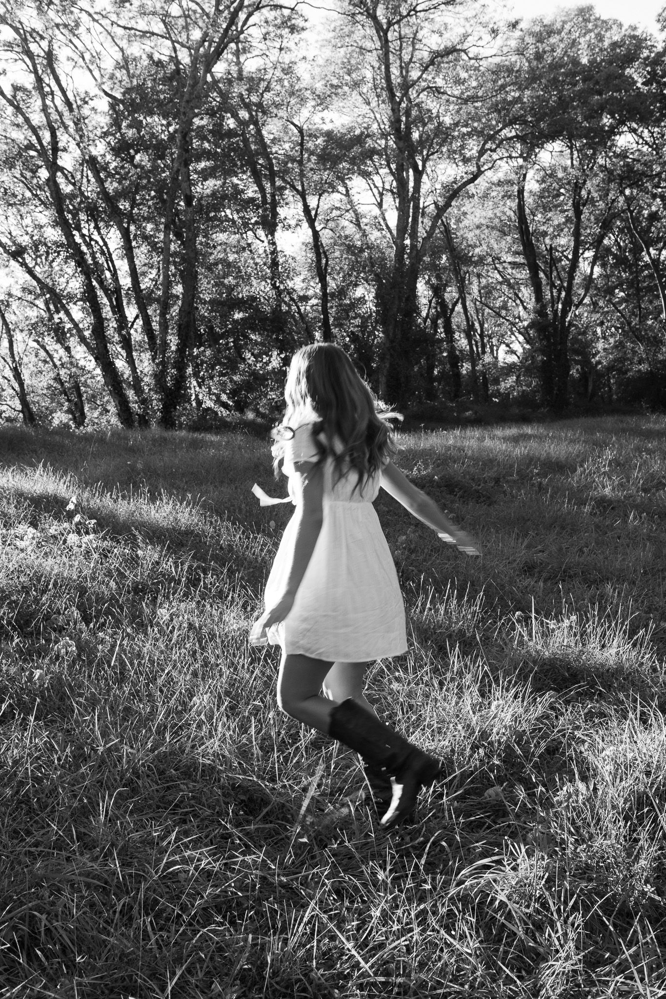 A person in a white dress twirls joyfully through a sunlit meadow in black and white photography.