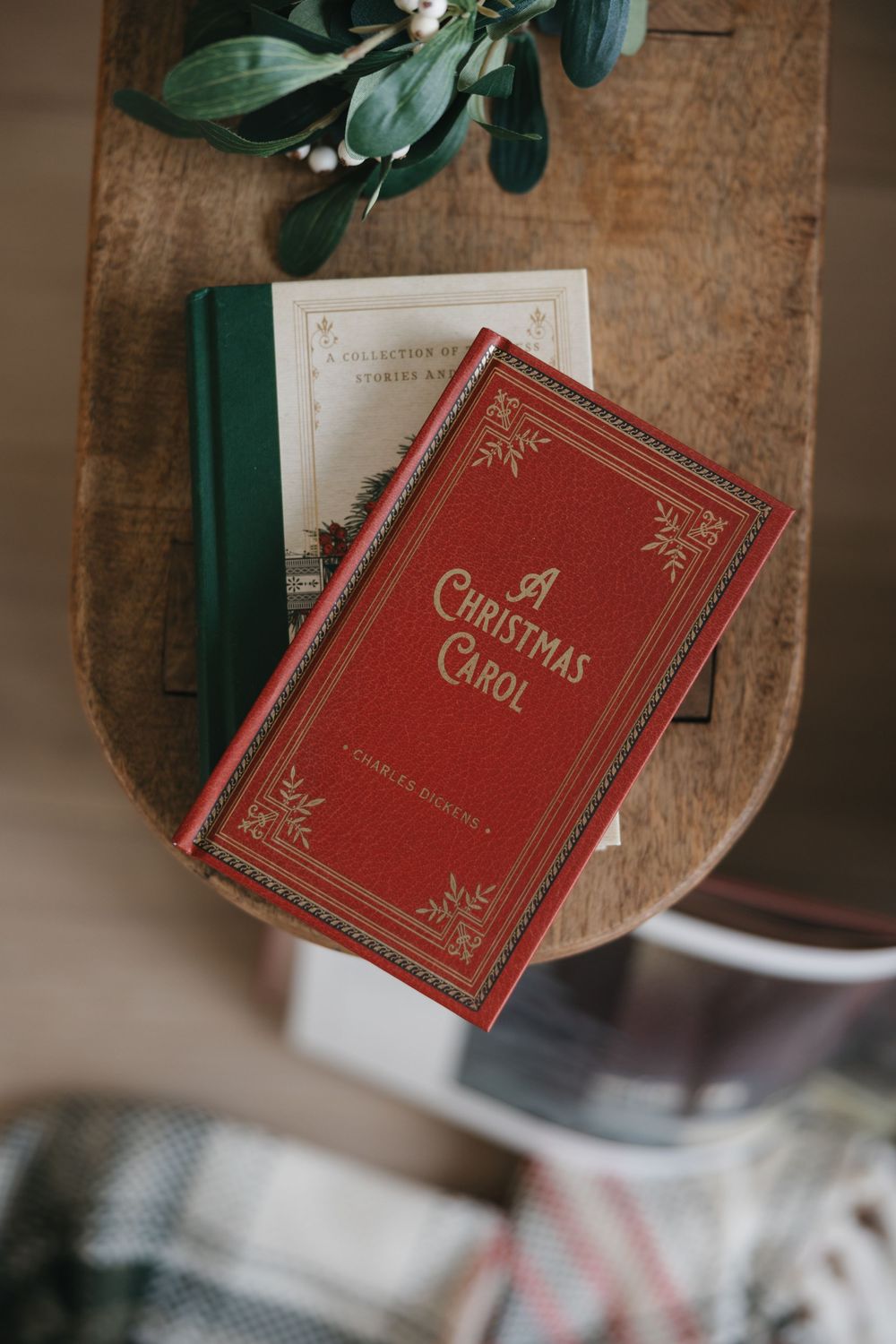 A red vintage Christmas carol book sits on a rustic wooden surface with green foliage in the background.