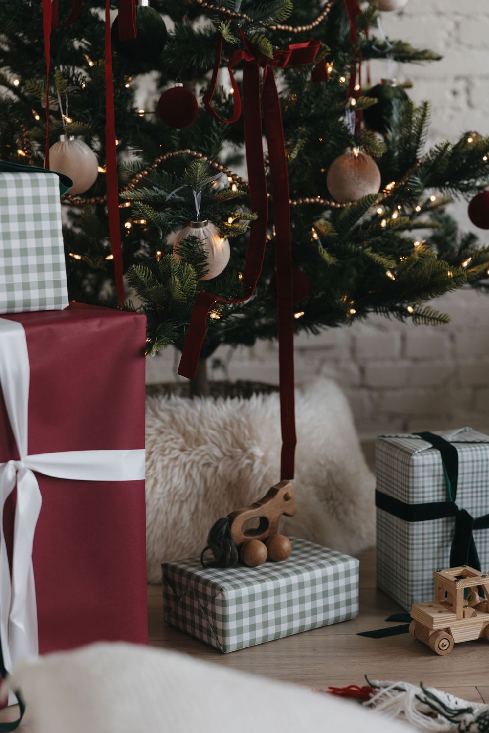 Wrapped Christmas presents in red and plaid paper sit under a decorated tree with gold ornaments and ribbons.