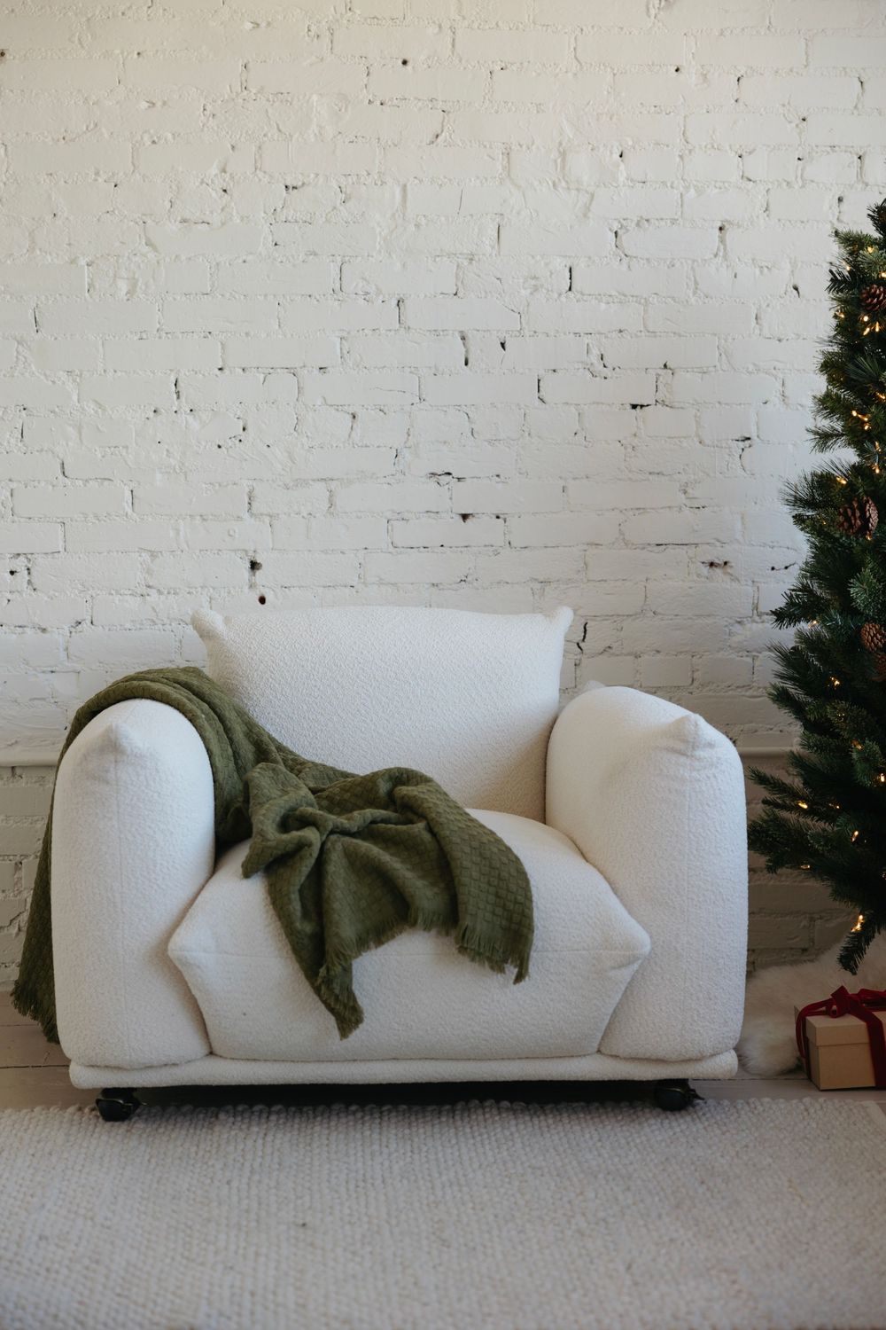 White modern sofa against painted brick wall with olive green throw blanket and partial view of Christmas tree.