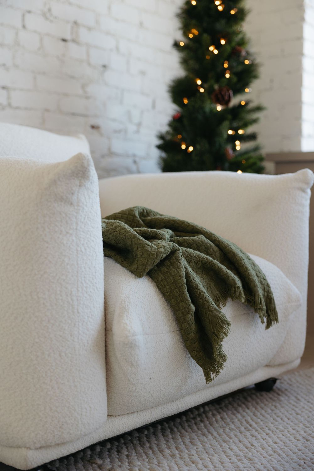 A cozy white couch with a green throw blanket near a decorated Christmas tree with twinkling lights.