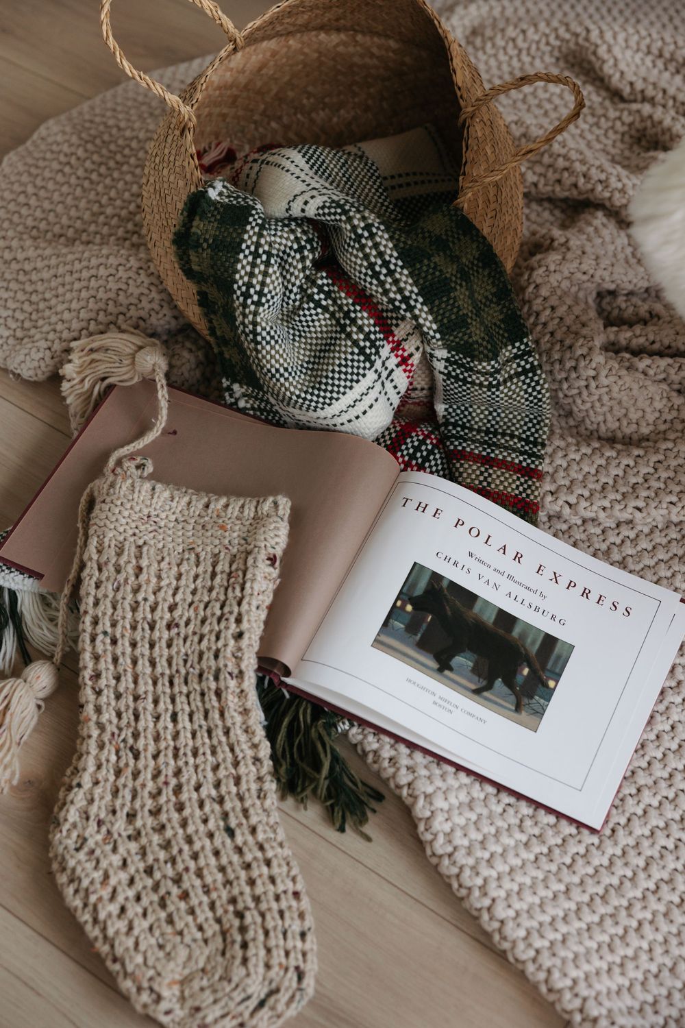 Cozy knit blankets and winter accessories arranged with coffee table books on a wooden surface.