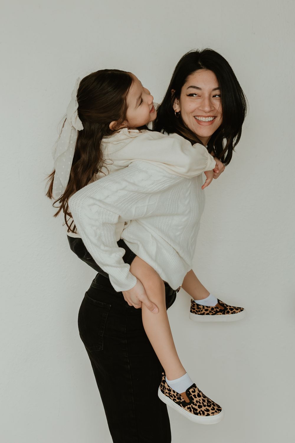 A woman in a white blouse and black pants dances and poses playfully against a white background.