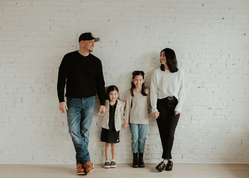 Family members walk together along a white wall in casual attire showing their feet and legs.