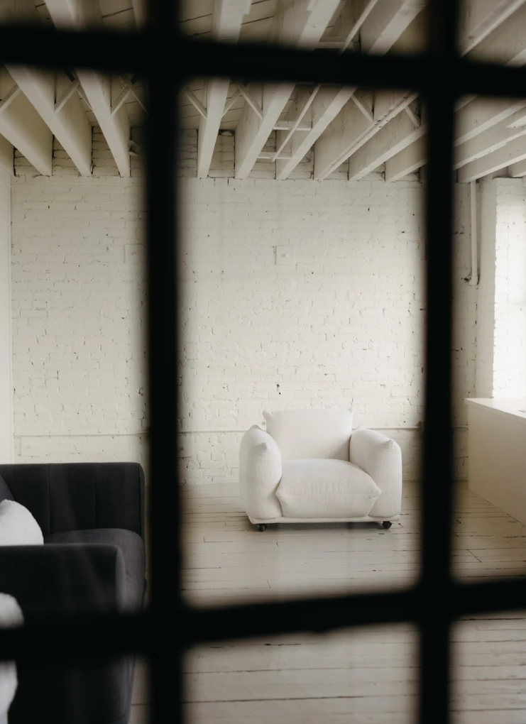 Interior view of an empty room with white walls and exposed ceiling beams seen through dark window frames.
