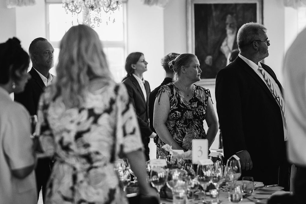 Black and white photo of guests mingling at an elegant dinner party with crystal glassware on tables.