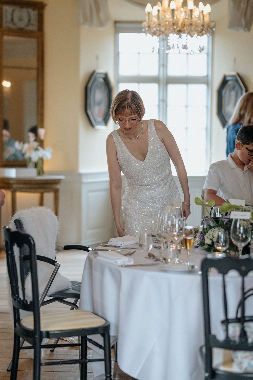 Elegant dining room with crystal chandelier, white tablecloths, and black chairs in a bright restaurant setting.