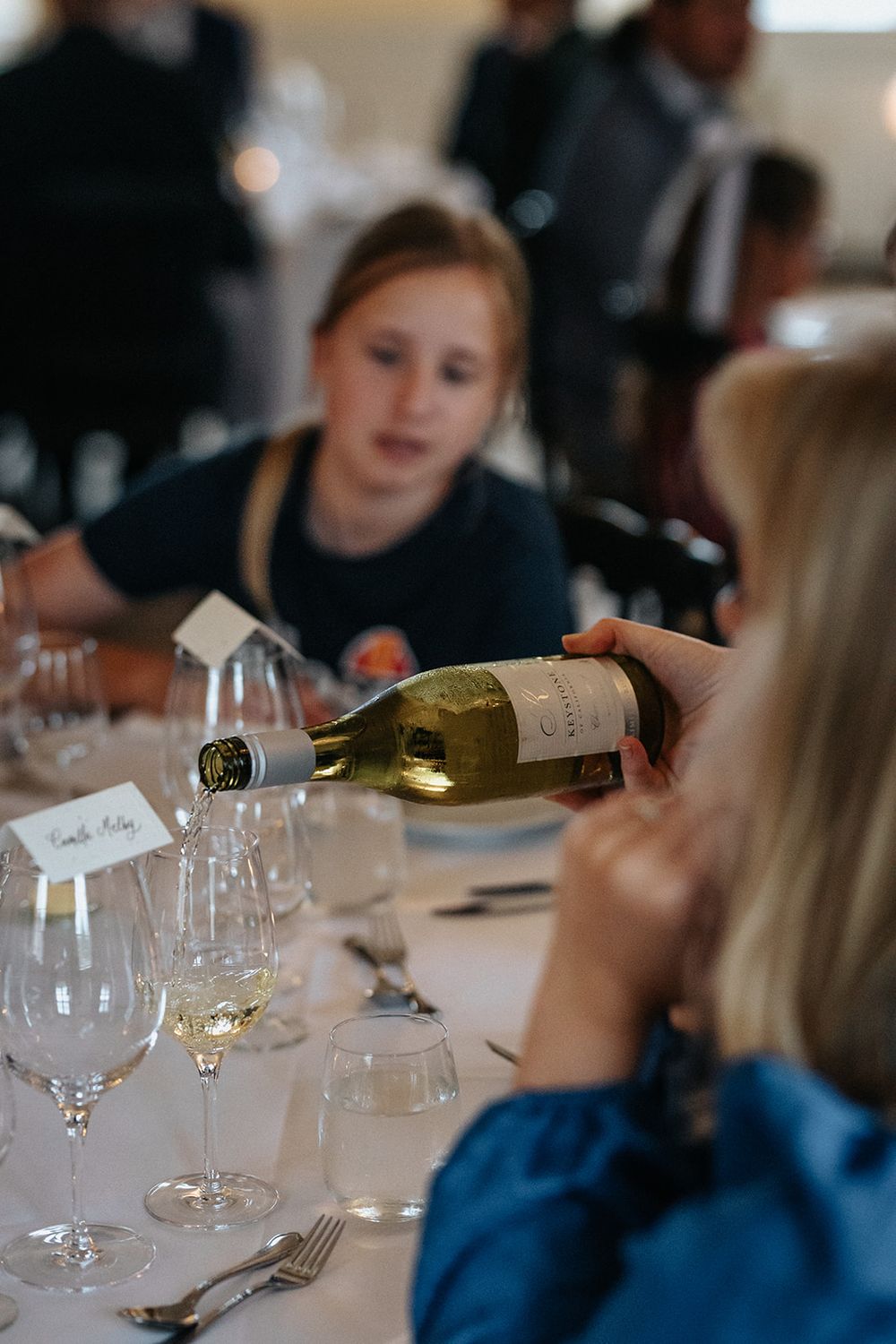 Wine is being poured into glasses at an elegant dining table during a tasting event.