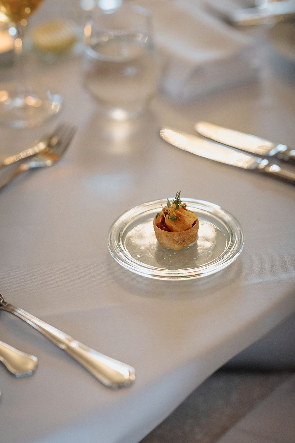 An elegant appetizer served on a glass plate with silverware on a white tablecloth in an upscale restaurant setting.