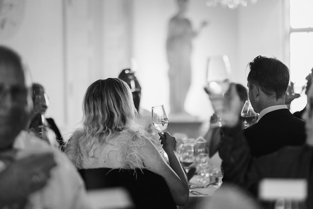Wedding guests enjoying a reception dinner in a dimly lit banquet hall with elegant table settings and glowing candlelight.