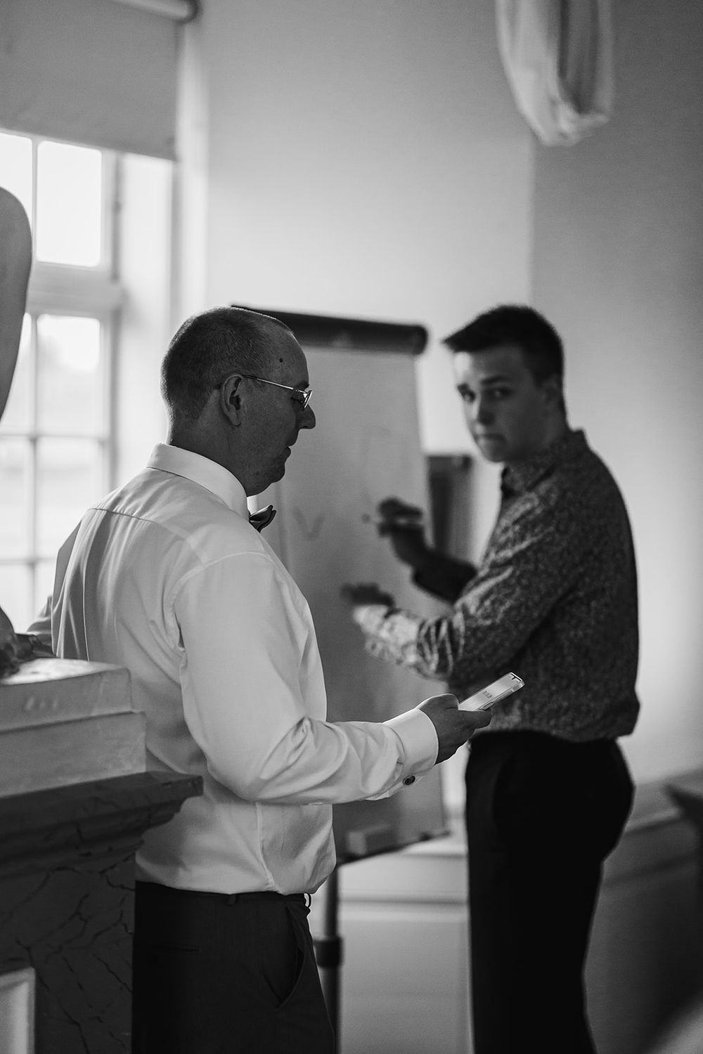 Two people practicing dance moves together in a bright indoor studio space, captured in black and white.
