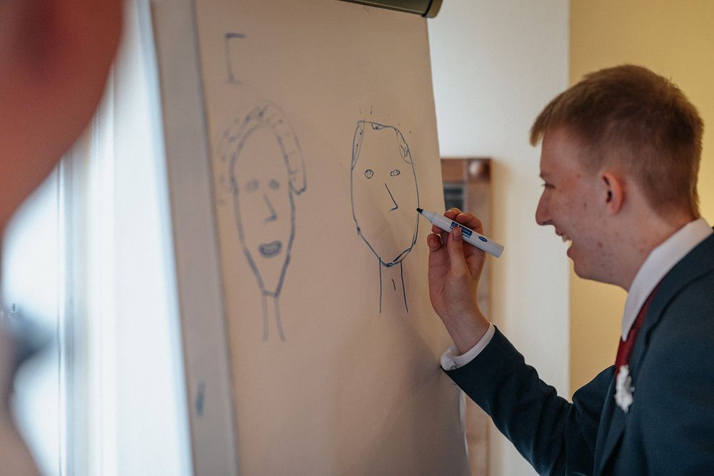 Someone in a suit draws simple face sketches on a whiteboard during a presentation or meeting.