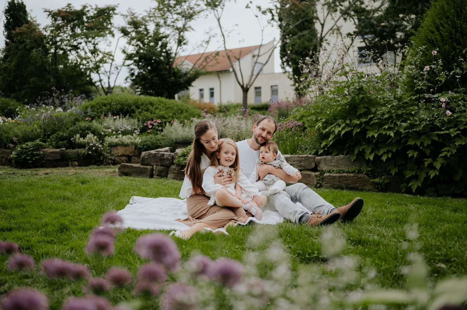 Ein Paar sitzt während einer Fotosession an einem sonnigen Nachmittag gemeinsam auf einer Decke in einem üppigen Garten.