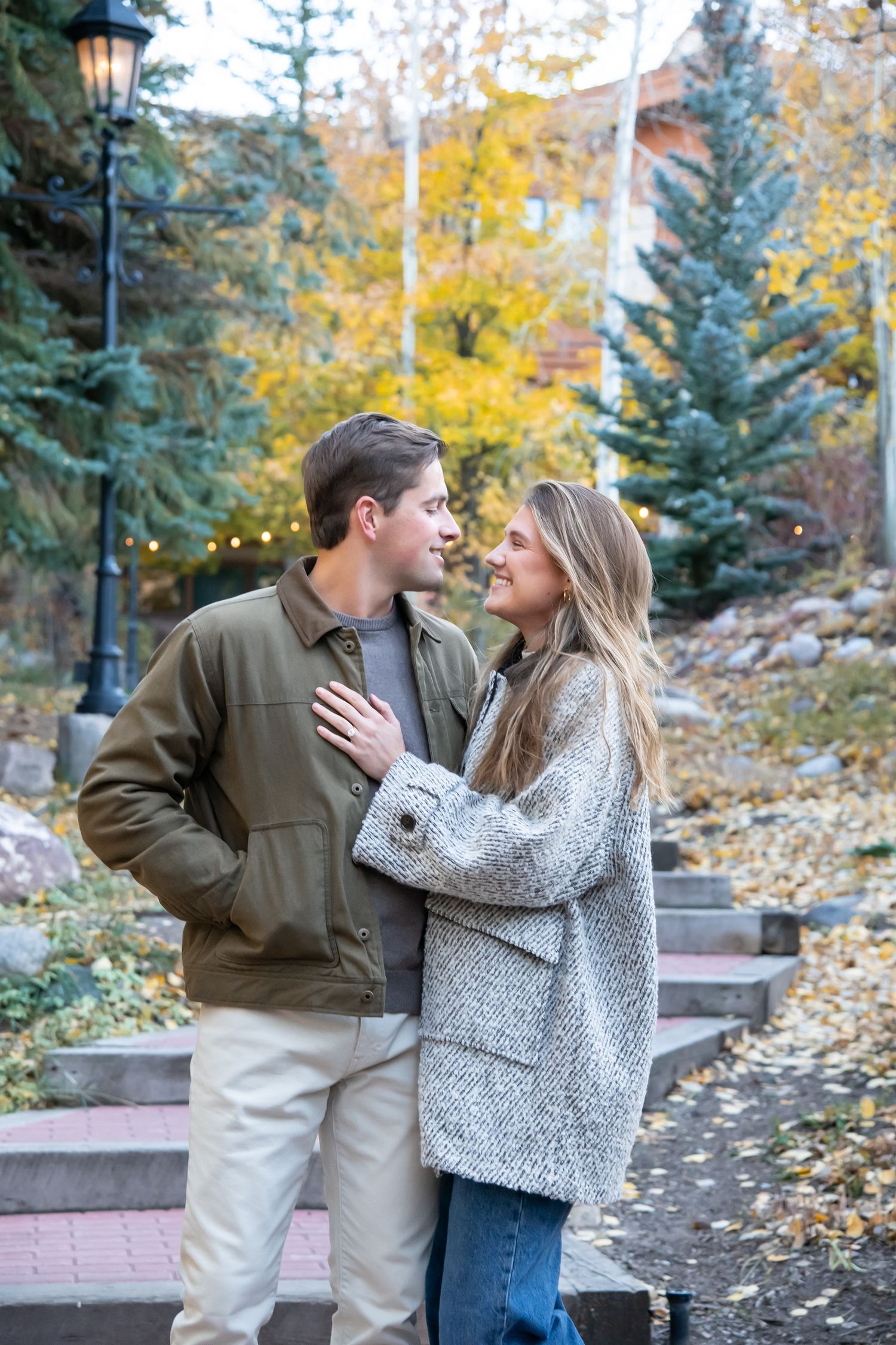 A cute couple shares tender moments in a scenic fall setting with evergreen trees and yellow foliage in the background in Vail Colorado