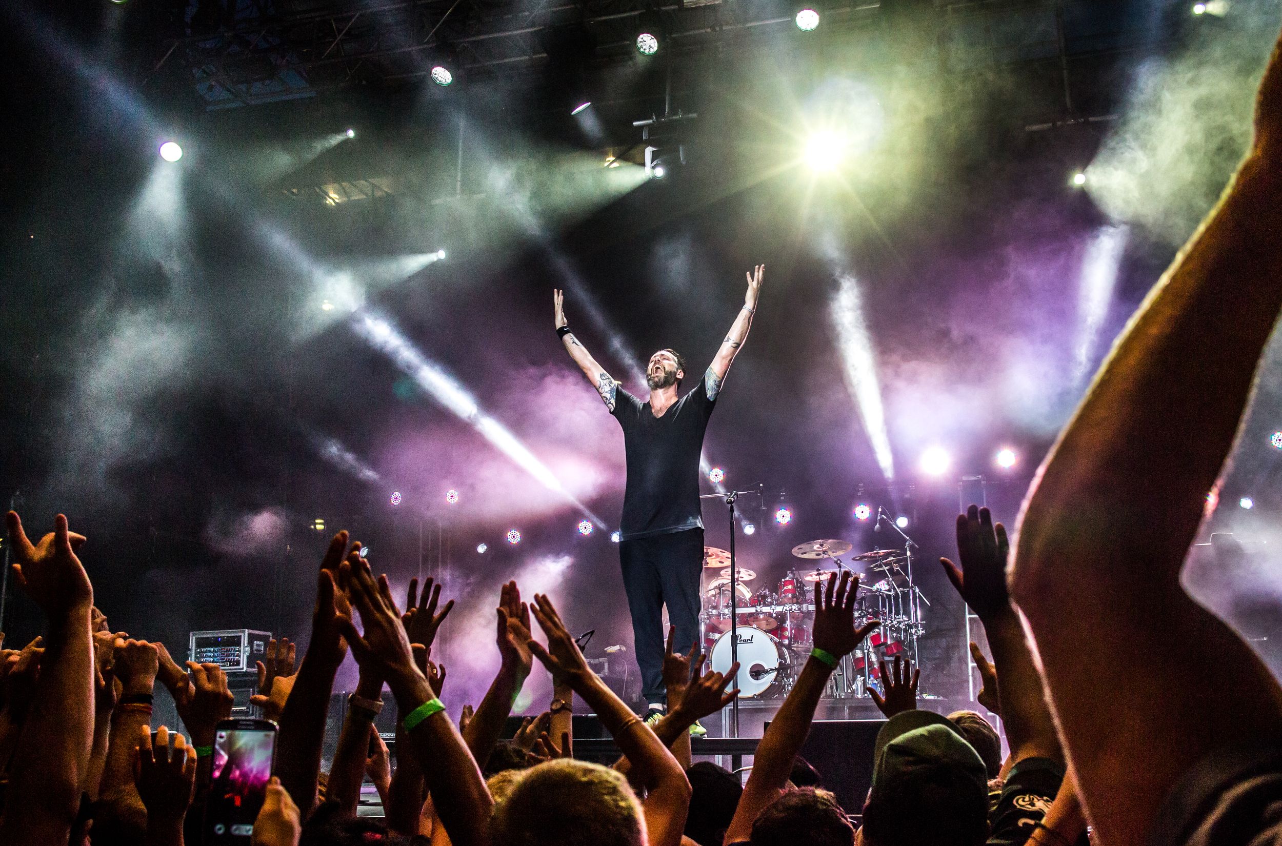 A concert performer silhouetted against bright stage lights with crowd raising hands.