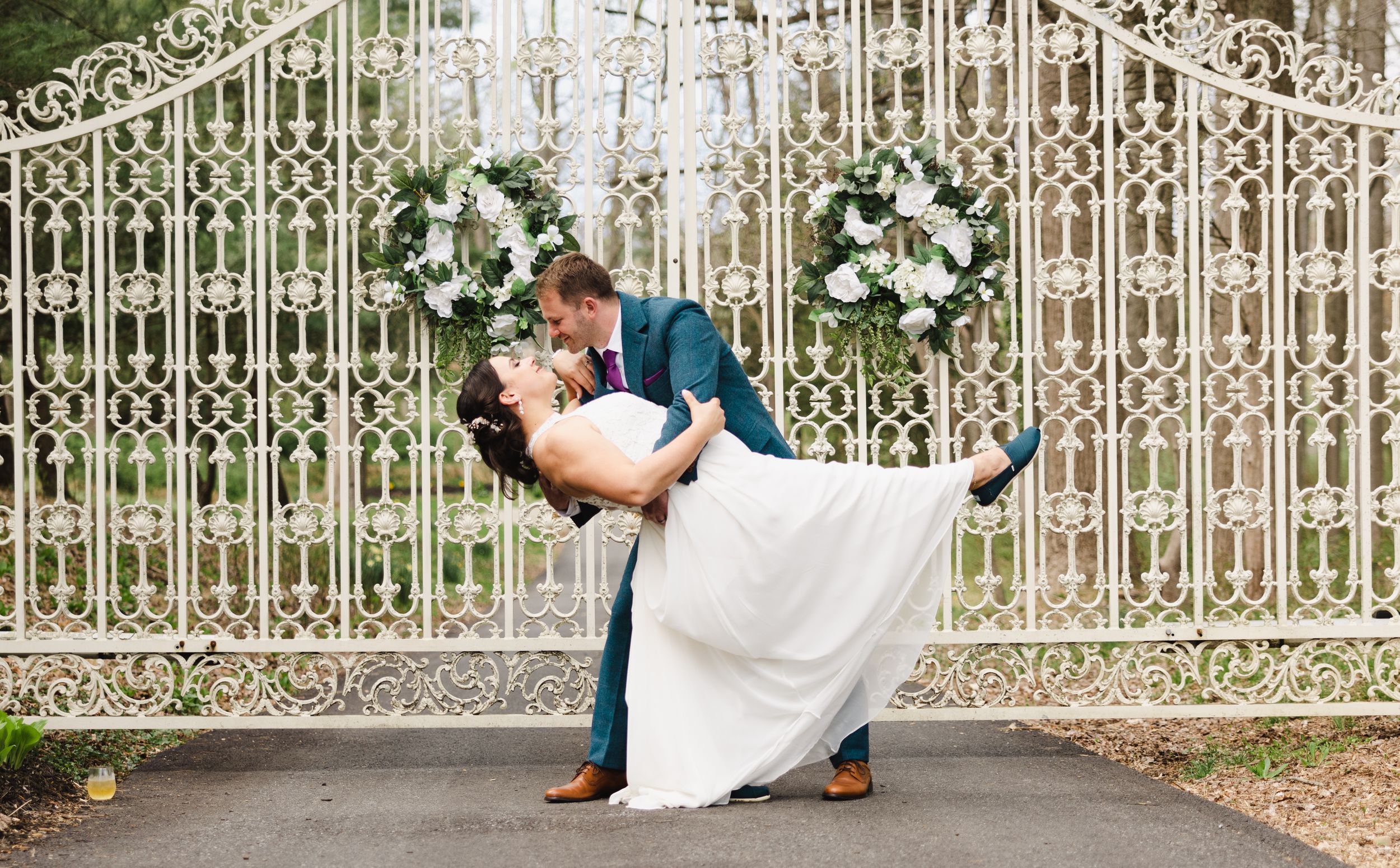 Ornate white iron gate entrance decorated with wedding floral arrangements.