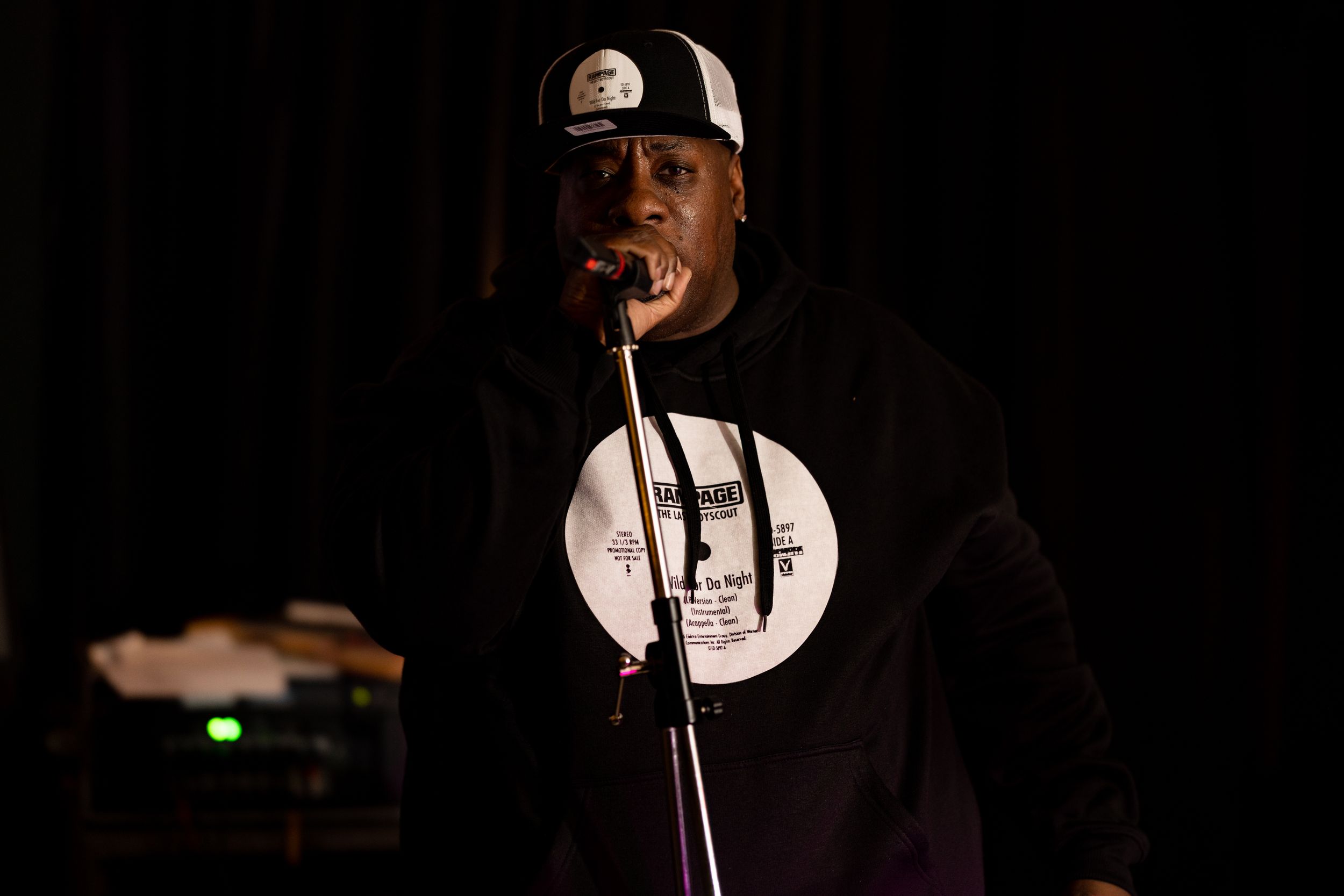 A performer singing into a microphone on a dark stage with dramatic lighting.