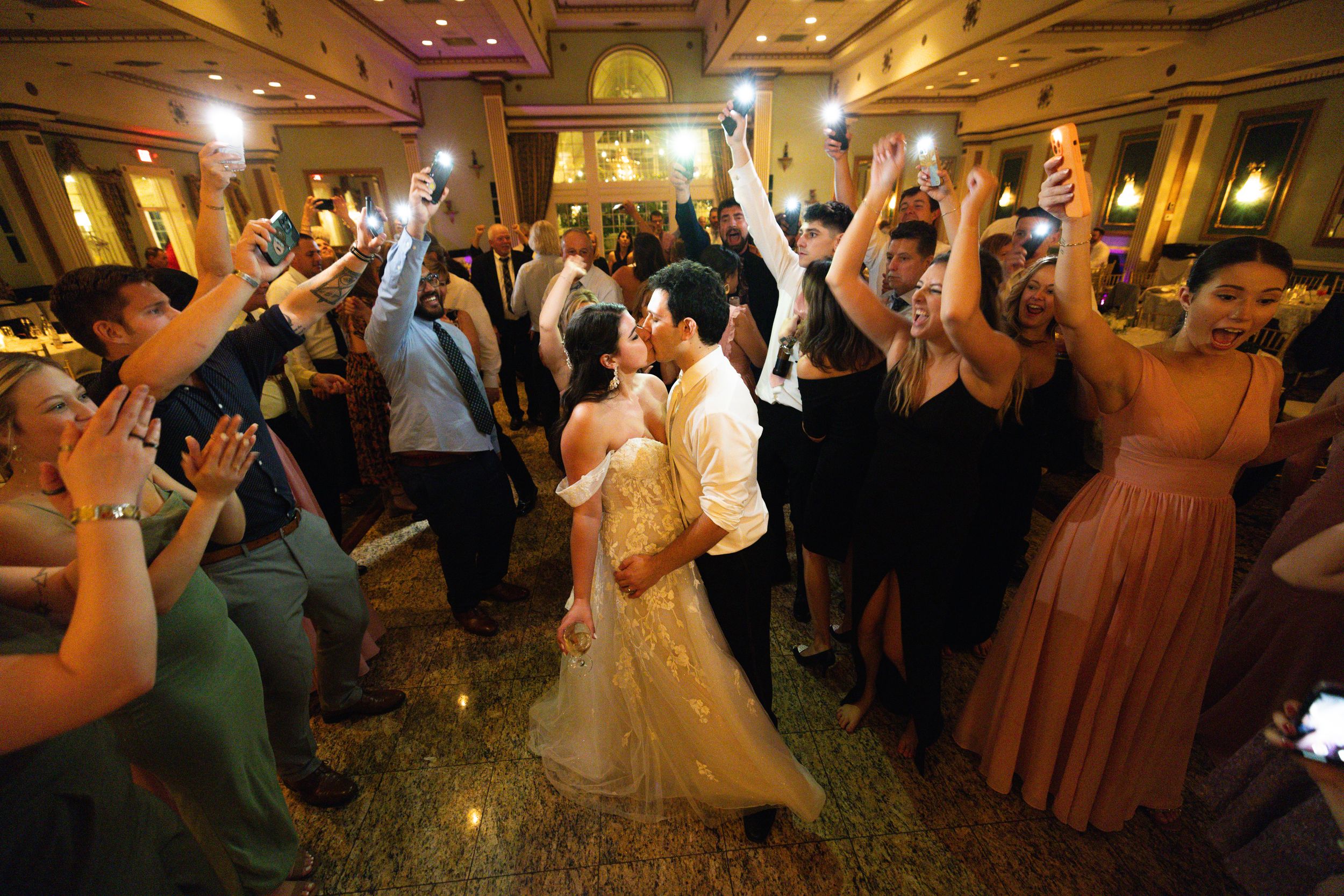 Wedding reception celebration with guests dancing under warm lighting.